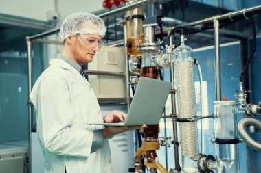 CBD yağ çıkarıcısının yanında dizüstü bilgisayarla çalışan eczacı bilim adamı ve tıbbi esrar ürünleri üretmek için kullanılan bilimsel bir makine.
