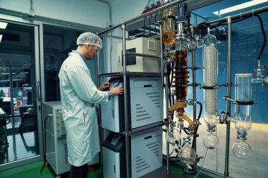 Bilim adamı ya da eczacı tıbbi ve sağlık hizmetleri için kenevir yağı çıkarıyor. Esrar ürünlerinden alınan sağlık hizmetleri eczanesi. Cam tüpler ve teçhizatlı kenevir yağı çıkarma makinesi.