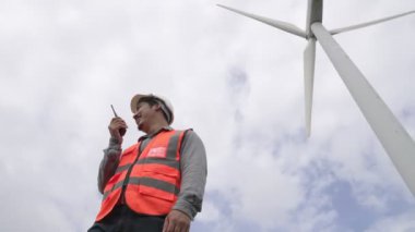 Gökyüzü arka planına sahip bir rüzgar türbini üzerinde çalışan mühendis. Yenilenebilir ve sürdürülebilir enerjinin gelecekteki üretimi için yenilikçi bir ideal. Rüzgar türbininden enerji üretimi.