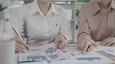 Ofis masasında çalışan iki hevesli genç iş kadını, veri tablosu raporlarıyla birlikte. Genç meslektaşlar istatistik veri kağıdı planları ve stratejisini tartışıyor ve analiz ediyorlar.