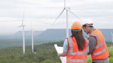 Erkek ve kadın mühendisler kırsal kesimdeki bir tepenin tepesinde ya da dağda rüzgar çiftliğinde çalışıyorlar. Yenilenebilir ve sürdürülebilir enerjinin gelecekteki üretimi için yenilikçi idealler.