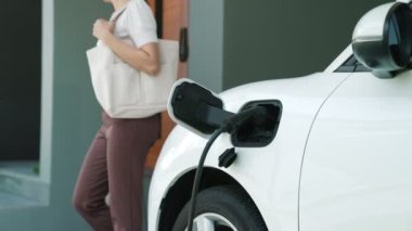 Bir kadın evinde elektrikli araç şarj aletinin fişini çekiyor. İlerici bir yaşam tarzında elektrikli araçların kullanımı, temiz ve sağlıklı bir çevreye katkıda bulunur..