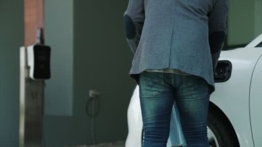 İlerici baba-kız elektrikli araç şarj istasyonundan fiş takıyor. Geleceğin çevre dostu arabası yenilenebilir temiz enerji kaynağıyla çalışıyor..