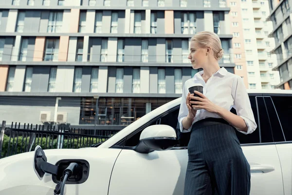 Businesswoman Drinking Coffee Leaning Electric Vehicle Recharging Public Charging Station — Foto de Stock