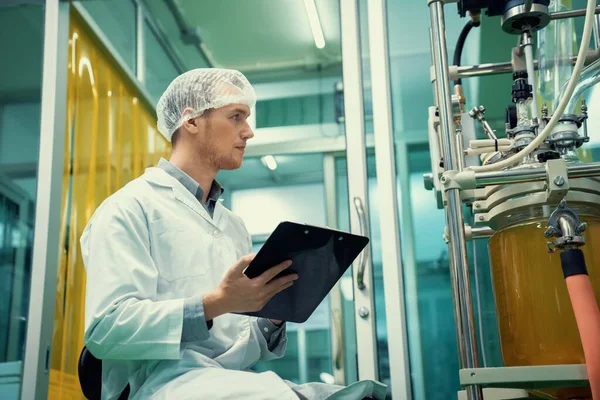 stock image Apothecary scientist using a clipboard and pen to record information from a CBD oil extractor and a scientific machine used to create medicinal cannabis products.