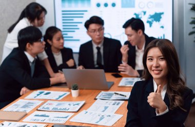 Focus portrait of female manger, businesswoman in the harmony meeting room with blurred of colleagues working together, analyzing financial paper report and dashboard data on screen in background.