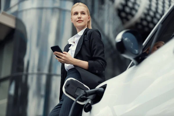 Businesswoman Wearing Black Suit Using Smartphone Leaning Electric Car Recharge — Fotografia de Stock