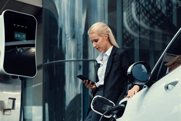 Businesswoman Wearing Black Suit Using Smartphone Leaning Electric Car Recharge — 图库照片