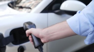 İlerici işadamı, şehir merkezinde dolaşmadan önce şarj cihazından elektrikli arabasına şarj prizi takıyor. Çevre dostu şarj edilebilir araba, sürdürülebilir ve temiz enerjiyle çalışıyor..
