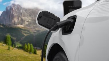 Temiz çevre için temiz enerjinin yol açtığı ilerici elektrikli araba kavramının arka planı olarak dağın tepesinde bulutun zaman kavramının yer aldığı doğal manzara. EV araba şarj istasyonunda şarj oluyor..