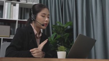 Kulaklık ve mikrofon takan iş kadını masasında çalışıyor ve dizüstü bilgisayar kullanıyor. Uzaktan kumandalı online toplantı için dizüstü bilgisayar kullanan hevesli kadın çalışanlar, ofiste iş videosu konferansı.