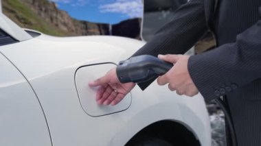 İş dünyasındaki ilerici adam elektrik yükleme istasyonundan doğal şelale ve akış geçmişi olan elektrikli araba giyer. Enerji sürdürülebilirliği kavramı.