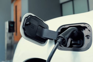 Closeup electric vehicle plugged-in with cable from charging point powered for progressive concept by alternative clean energy rechargeable EV car at home charging station.