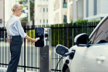 Credit card payment for eco-friendly clean and sustainable energy for electric vehicle at charging station. Progressive woman pay for charging point to power his electric rechargeable vehicle.