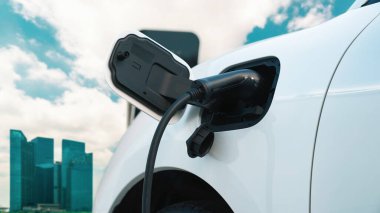 Elektrikli araç, EV araba şehir merkezindeki şarj istasyonunda şarj oluyor. Etrafı yüksek gökdelenlerle çevrili. Çevre dostu yenilikçi temiz enerji kavramı.