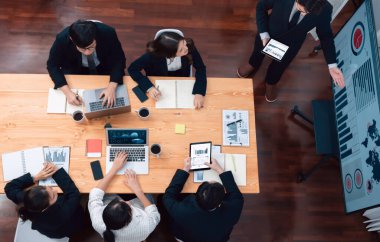 Top view manager or office worker give presentation in harmony conference room to business colleague, BI data dashboard on screen and pile of financial analyzed data reports on meeting table.