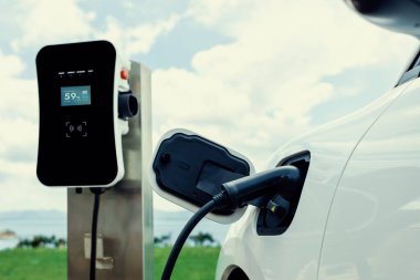 Progressive concept of electric vehicle, EV car alongside with charging station. Natural background of green field for clean environment for eco-car with renewable energy concept.