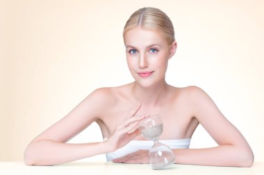 Personable model holding hourglass in beauty concept of anti-aging skincare treatment for woman. Young girl portrait with perfect smooth clean skin and flawless soft makeup in isolated background.