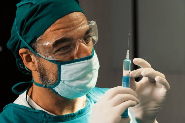 Cerrah steril ameliyathanede cerrahi prosedür için tıbbi şişeden şırınga dolduruyor. Ameliyat için koruyucu giysisi olan doktor hastasına anestezi iğnesi hazırlayın.