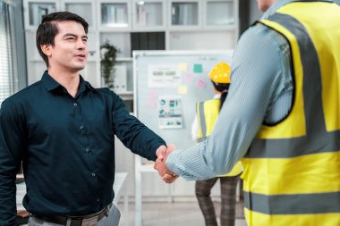 An engineer with a protective vest handshake with an investor in his office. Following a successful meeting, employee and employer form a partnership.