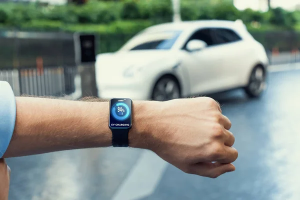Closeup focus progressive wearable watch show electric car battery status that being recharge at charging station point in the city. Digital interface, data from EV car display on smartwatch.