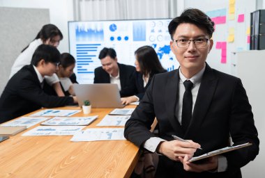 Focus portrait of successful confident male manager or executive in business wear with blurred background of businesspeople, colleagues working with financial report papers in office of harmony.