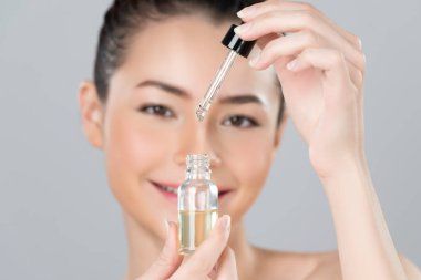Focus cannabis extracted oil bottle with dropper lid holding by blurred glamorous beautiful asian woman with perfect clean skin and soft smooth makeup in isolated background.