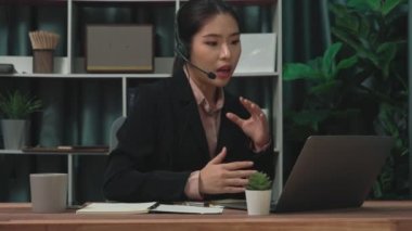 Kulaklık ve mikrofon takan iş kadını masasında çalışıyor ve dizüstü bilgisayar kullanıyor. Uzaktan kumandalı online toplantı için dizüstü bilgisayar kullanan hevesli kadın çalışanlar, ofiste iş videosu konferansı.
