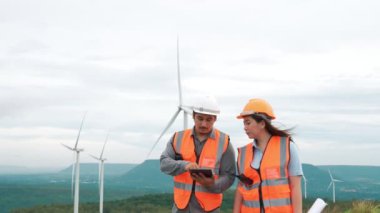 Erkek ve kadın mühendisler kırsal kesimdeki bir tepenin tepesinde ya da dağda rüzgar çiftliğinde çalışıyorlar. Yenilenebilir ve sürdürülebilir enerjinin gelecekteki üretimi için yenilikçi idealler.