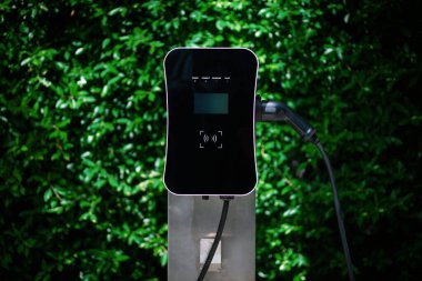 Charging station with greenery foliage background for combination of nature and alternative energy for progressive future renewable energy for electric car. Charger point with connecter device.