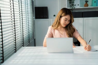 A young Asian female employee sitting at her desk in her office, sitting at desktop in workstation.