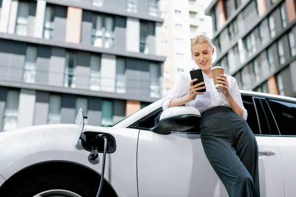 Focus Businessman Using Phone Leaning Electric Vehicle Holding Coffee Blurred — Stockfoto