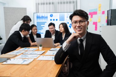 Focus portrait of successful confident male manager or executive in business wear with blurred background of businesspeople, colleagues working with financial report papers in office of harmony.