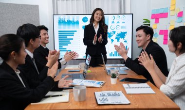 Confidence and young asian businesswoman give presentation on financial business strategy in dashboard report display on screen to colleagues in conference room meeting as harmony in workplace concept