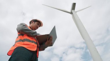 Gökyüzü arka planına sahip bir rüzgar türbini üzerinde çalışan mühendis. Yenilenebilir ve sürdürülebilir enerjinin gelecekteki üretimi için yenilikçi bir ideal. Rüzgar türbininden enerji üretimi.