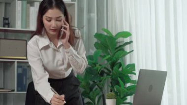 Genç hevesli iş kadını iş görüşmesinde konuşuyor ve masasına dizüstü bilgisayarla bir not yazıyor. Kadın çalışan telefonda konuşuyor ve ofis evraklarına iş ödevi yazıyor..