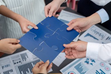 Closeup top view business team of office worker putting jigsaw puzzle together over table filled with financial report paper in workplace with manager to promote harmony concept in meeting room.