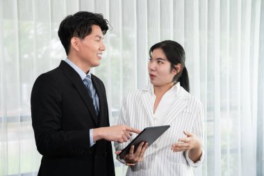 Manager advising guiding younger colleague with tablet in workplace. Couple businesspeople in formal wear working together on financial strategy as concept of teamwork and harmony in office.