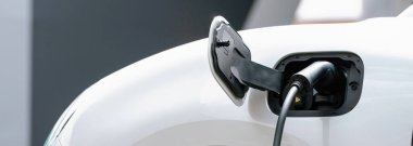 Closeup electric vehicle plugged-in with cable from charging point powered for progressive concept by alternative clean energy rechargeable EV car at home charging station.
