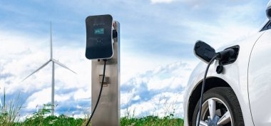 Progressive combination of wind turbine and EV car, future energy infrastructure. Electric vehicle being charged at charging station powered by renewable energy from wind turbine in the countryside.