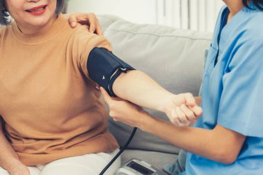 An elderly woman with a contented life having a blood pressure check by her caregiver at home with a smiley face.