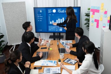 Confidence and young asian businesswoman give presentation on financial business strategy in dashboard report display on screen to colleagues in conference room meeting as harmony in workplace concept