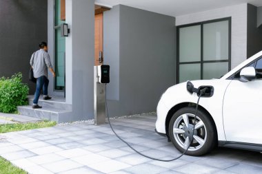 Progressive asian man and electric car with home charging station. Concept of the use of electric vehicles in a progressive lifestyle contributes to a clean and healthy environment.