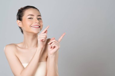 Glamorous beautiful woman with perfect makeup clean skin pointing finger in copyspace isolated background. Promotion indicated by hand gesture concept for skincare product advertisement.