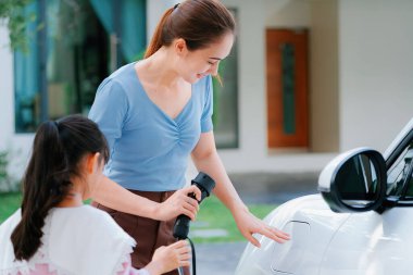 Evde şarj edilen elektrikli bir araçla okuldan yeni dönen anne ve kızın ilerici yaşam tarzı. Elektrikli araç, sürdürülebilir temiz enerjiyle çalışıyor..