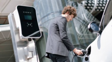 Below view closeup image of progressive black suit businessman recharge battery of his electric vehicle from public charging station. Renewable and alternative energy powered car concept.