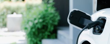 Closeup electric vehicle plugged-in with cable from charging point powered for progressive concept by alternative clean energy rechargeable EV car at home charging station.