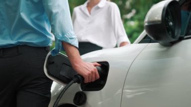 İlerici işadamı ve iş kadını, şehir merkezinde dolaşmadan önce şarj cihazını şarj istasyonundan elektrikli arabaya takıyor. Çevre dostu şarj edilebilir araba temiz enerjiyle çalışıyor..