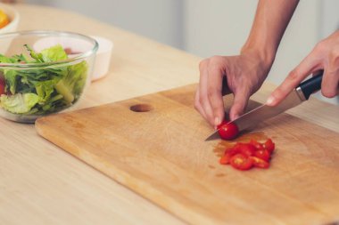 Close up hands holding a knife preparing a contented meal. Sliced tomatoes and other vegetables on the glass dish.