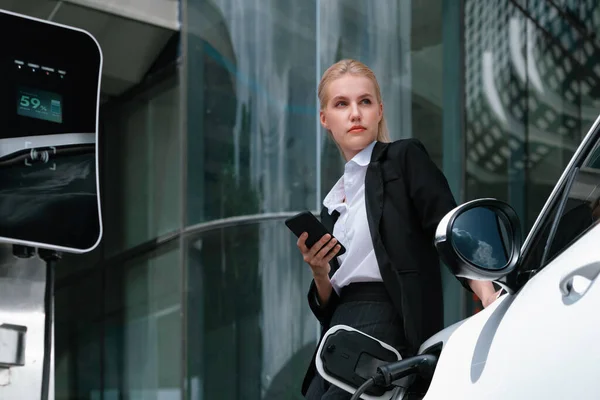 Businesswoman Wearing Black Suit Using Smartphone Leaning Electric Car Recharge — Stock Photo, Image
